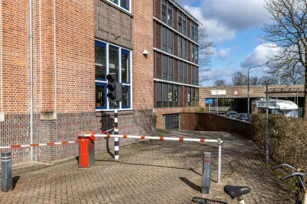 Ingang van een ondergrondse parkeergarage aan de Lage Naarderweg, met slagboom, verkeerslicht en omringende kantoorgebouwen.